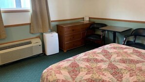 Ein Motelzimmer mit Bett, Kommode, Schreibtisch, Stühlen, einem Fernseher und einem Fenster mit Vorhängen.
