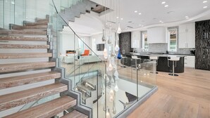 Une cuisine moderne dotée d’un îlot central, de rampes en verre et de luminaires suspendus.