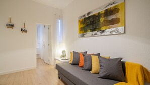 Una sala moderna con un sofá gris, una manta amarilla y un cuadro abstracto grande en la pared.