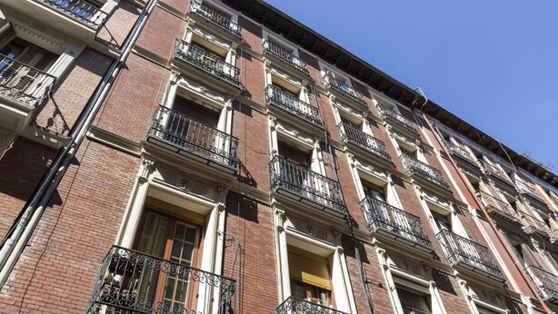Un edificio de varios pisos con fachadas de ladrillo, múltiples balcones con barandillas de hierro forjado y un cielo azul despejado.