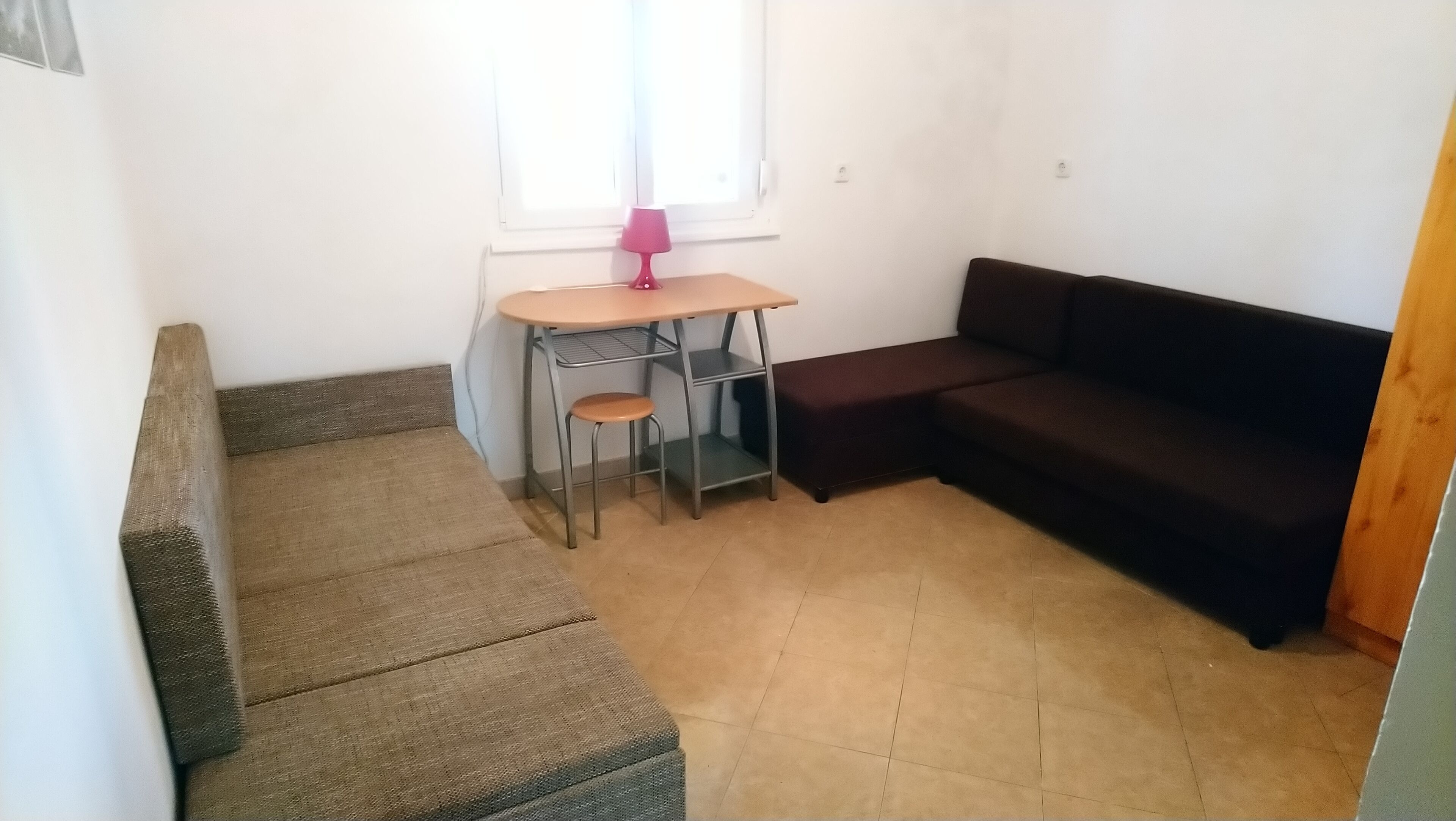 Ein kleiner, kompakter Wohnraum mit einer Couch, einem Tisch und einem Stuhl sowie einem Fenster mit Vorhängen.
