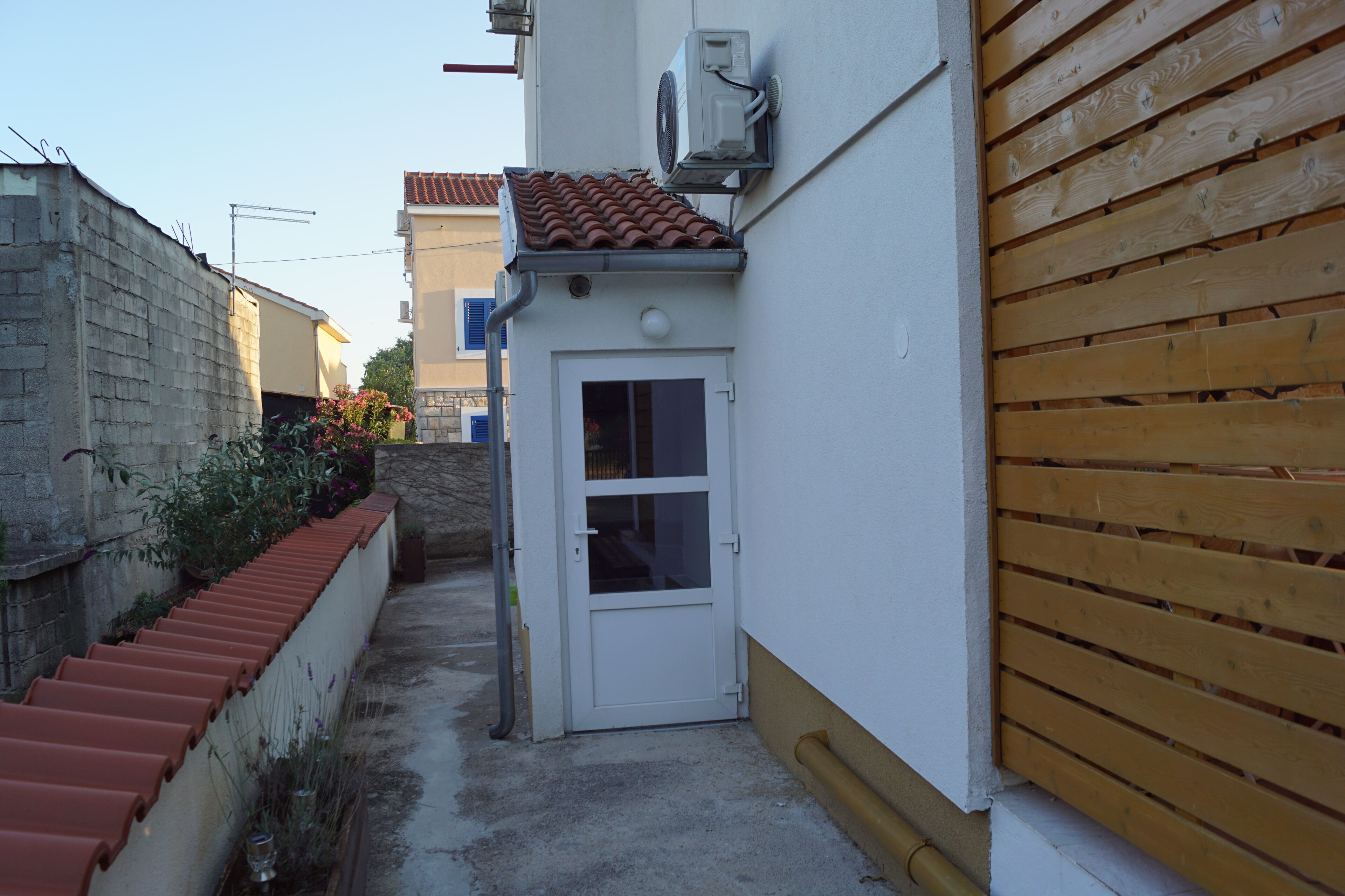 Une ruelle étroite avec une petite porte, un toit recouvert de tuiles et une clôture en bois.
