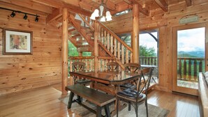 A wooden interior with a dining area featuring a glass table and chairs, a staircase, and a view of the outdoors. - Bella Yani - Hot Tub, Pool Table, & Air Hockey! (Sevierville)