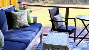 Un patio techado con un sofá azul, una silla de mimbre y una pequeña mesa.