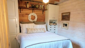 Un dormitorio acogedor con cama, cómoda, estante con adornos y una pared con un cuadro enmarcado.