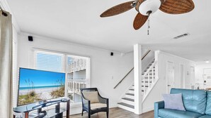 Un salon moderne doté d’un téléviseur à écran plat, d’un ventilateur de plafond, d’un canapé bleu et d’un escalier menant à un autre niveau.
