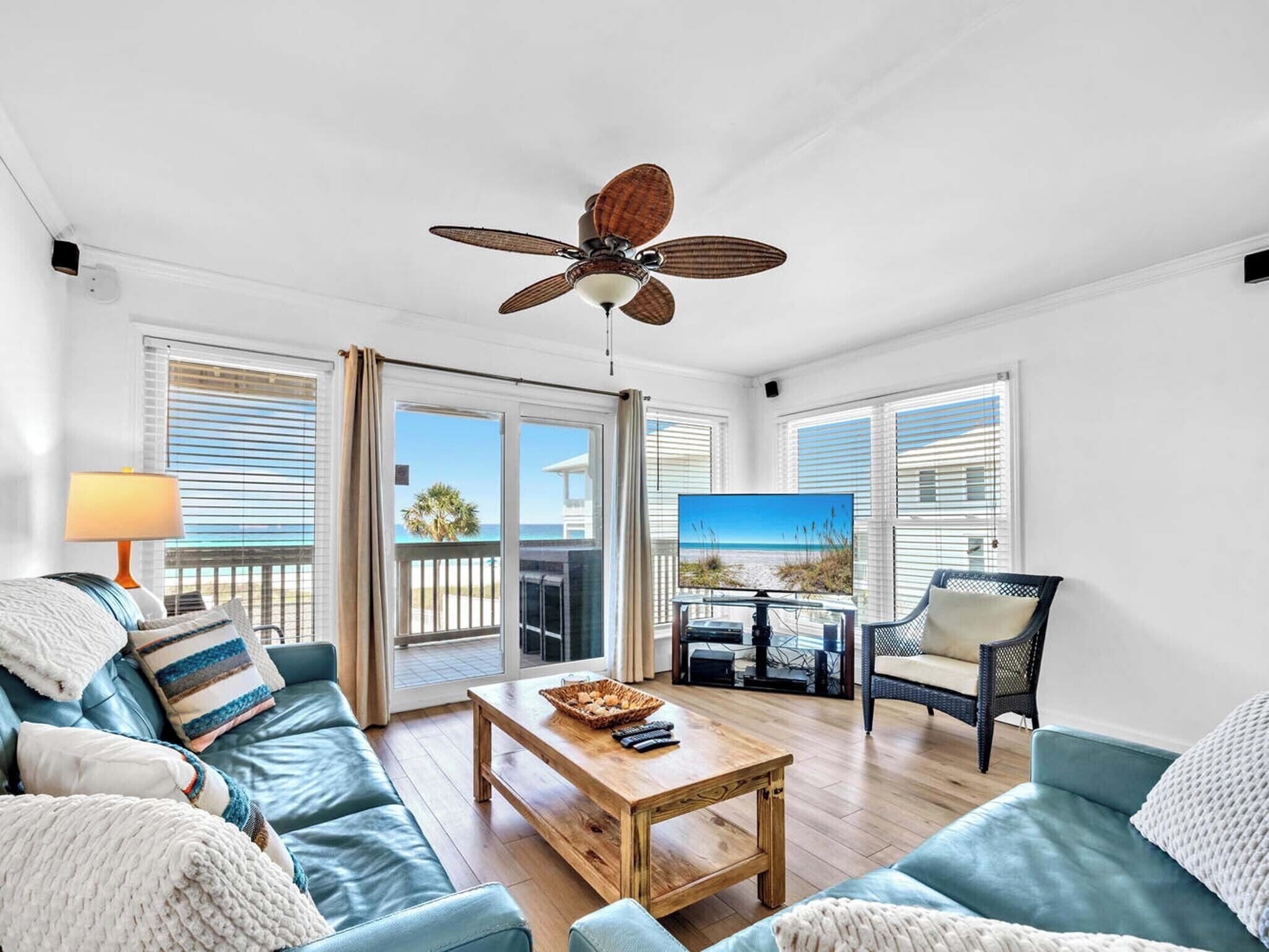 A spacious living room with a ceiling fan, a wooden coffee table, a blue sofa, a wicker chair, and a television.
