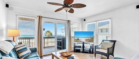 A spacious living room with a ceiling fan, a wooden coffee table, a blue sofa, a wicker chair, and a television.