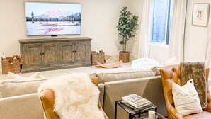 Un soggiorno con divano, due poltrone in pelle, televisore, mobile contenitore e finestra con tende.