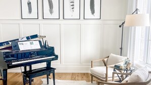 Una stanza con un pianoforte a coda, un tappeto in pelle, un divano bianco e opere d'arte con piume appese al muro.