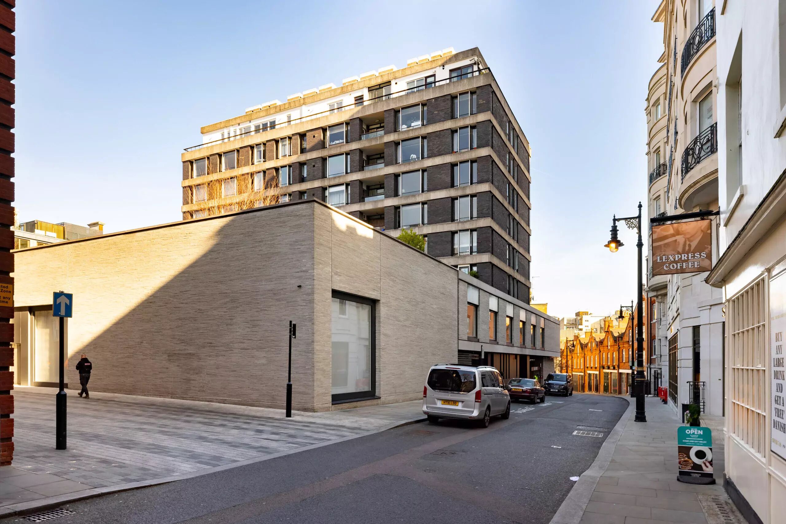 Un bâtiment moderne doté d’un toit plat et de grandes fenêtres, un fourgon garé dans la rue et une enseigne indiquant un café.