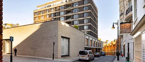 Un bâtiment moderne doté d’un toit plat et de grandes fenêtres, un fourgon garé dans la rue et une enseigne indiquant un café.