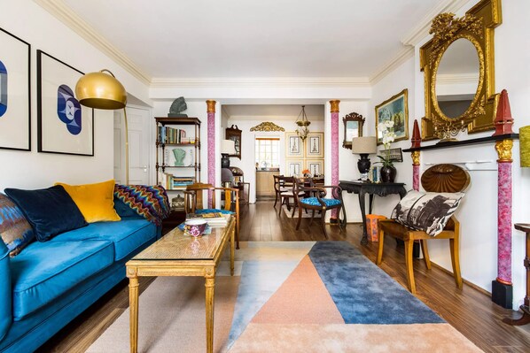 A living room with a blue sofa, a coffee table, a bookshelf, and a fireplace with a mirror.