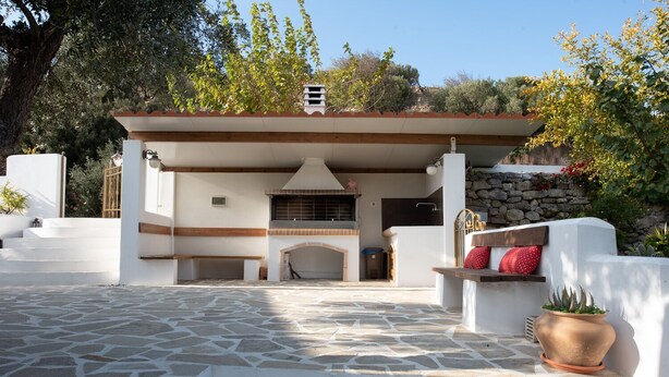 A covered outdoor area with a stone floor, a fireplace, and a seating bench.