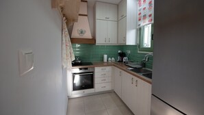 A kitchen with white cabinets, a stainless steel oven, a sink, and a window with a green-tiled backsplash.