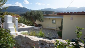 A courtyard with a stone floor, a white bench, and a small garden with plants and flowers.