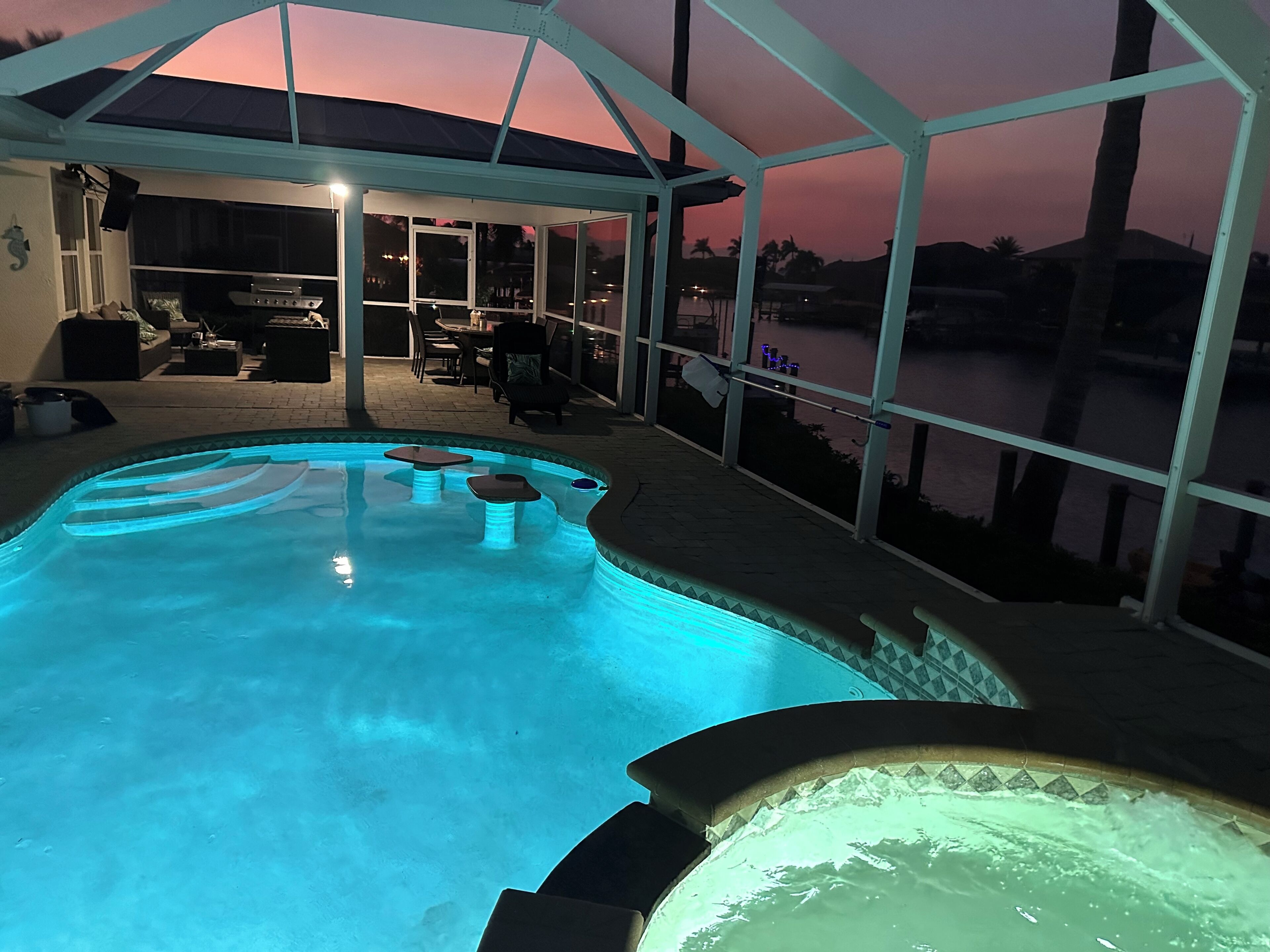 A swimming pool with a hot tub, surrounded by a covered patio area with seating and a view of the water.