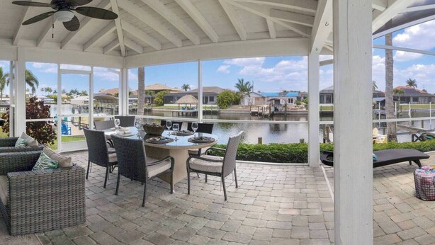 A covered patio with a table set for dining, overlooking a body of water and a residential area. - SW CAPE CORAL: 5 BR 4 BA CANAL HOME with BOAT DOCK  w/heated / lit pool, jacuzzi (Cape Coral)
