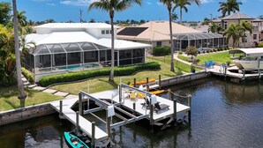 A waterfront property with a dock, a swimming pool, and a covered outdoor area. - SW CAPE CORAL: 5 BR 4 BA CANAL HOME with BOAT DOCK  w/heated / lit pool, jacuzzi (Cape Coral)