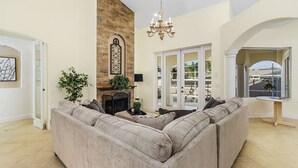 A spacious living room with a large beige sectional sofa, a fireplace, and a chandelier. - Sophisticated Style- Pool, Outdoor Bar, minutes to downtown Cape Coral- Villa Tuscany - Roelens (Cape Coral)