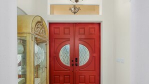 A red double door with glass panels and a decorative cabinet to the left. - Sophisticated Style- Pool, Outdoor Bar, minutes to downtown Cape Coral- Villa Tuscany - Roelens (Cape Coral)