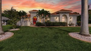A house with a well-maintained lawn, palm trees, and a sunset sky. - Sophisticated Style- Pool, Outdoor Bar, minutes to downtown Cape Coral- Villa Tuscany - Roelens (Cape Coral)