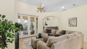 A spacious living room with a beige sectional sofa, a chandelier, and a large window. - Sophisticated Style- Pool, Outdoor Bar, minutes to downtown Cape Coral- Villa Tuscany - Roelens (Cape Coral)