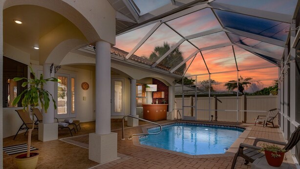 An indoor swimming pool with a glass ceiling, surrounded by lounge chairs and a brick floor. - Sophisticated Style- Pool, Outdoor Bar, minutes to downtown Cape Coral- Villa Tuscany - Roelens (Cape Coral)