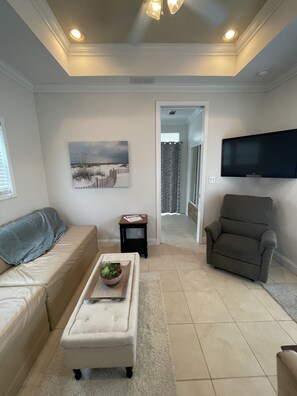 Relax in this inviting living room with a beige sofa, white ottoman, and flat-screen TV.