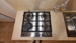 Une cuisine équipée d’une cuisinière à gaz à quatre brûleurs, d’un évier en acier inoxydable et d’un dosseret carrelé.