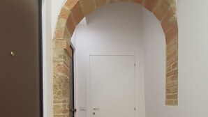 Un couloir avec une porte marron, une porte blanche et une arche en briques. On y trouve deux paillassons noirs sur le sol.