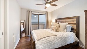 Een slaapkamer met een houten hoofdbord, een bed met wit beddengoed, een plafondventilator en een raam met gordijnen.