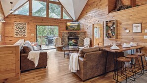 A spacious cabin with a high ceiling, wooden walls, a fireplace, and a dining area with bar stools.