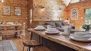 A wooden cabin interior with a dining area, wooden walls, and a large window.
