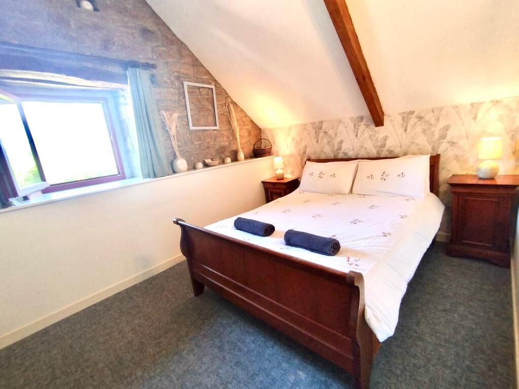 Un dormitorio con una cama de madera, una ventana, una pared de piedra y una mesita de noche con lámpara.