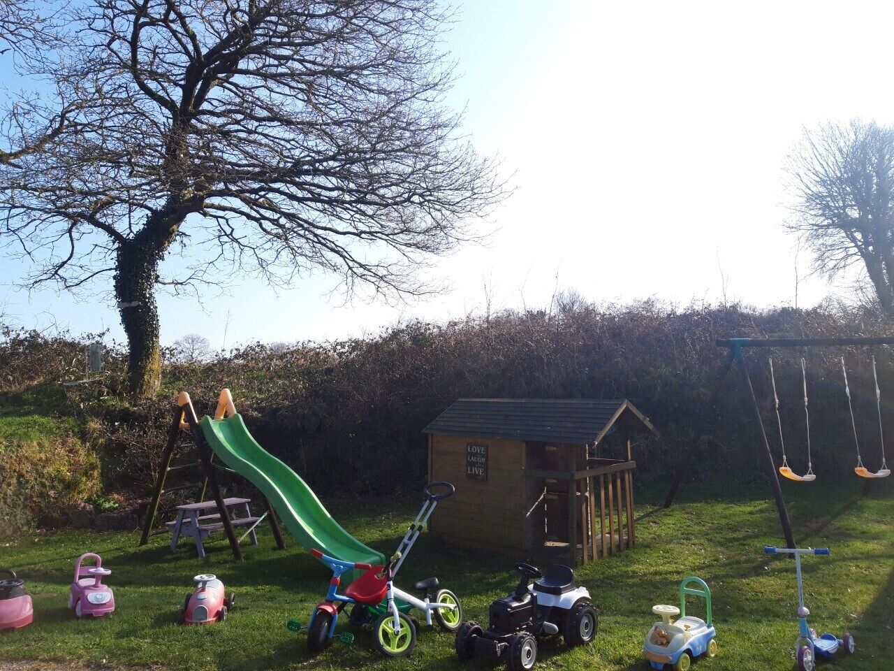 A playground with a slide, swings, and a small shed with a sign that says "LOVE LAUGH LIVE".