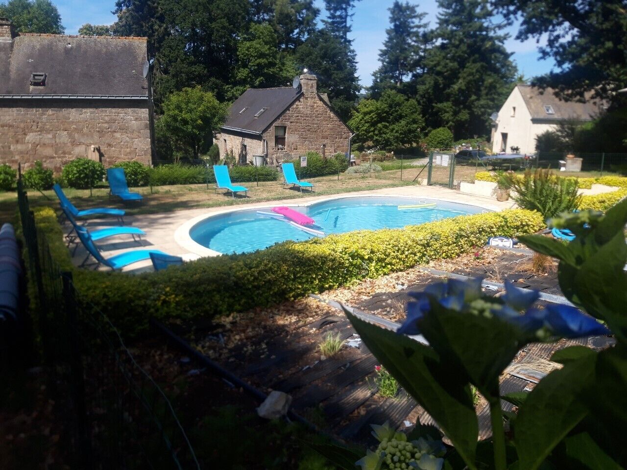 Ein Garten mit Schwimmbad, blauen Liegestühlen und Gebäuden aus Stein.