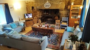 A cozy living room with a stone fireplace, a television, and a wooden cabinet with glass doors. - ----Breton hamlet 20 persons---- (LANGOELAN)