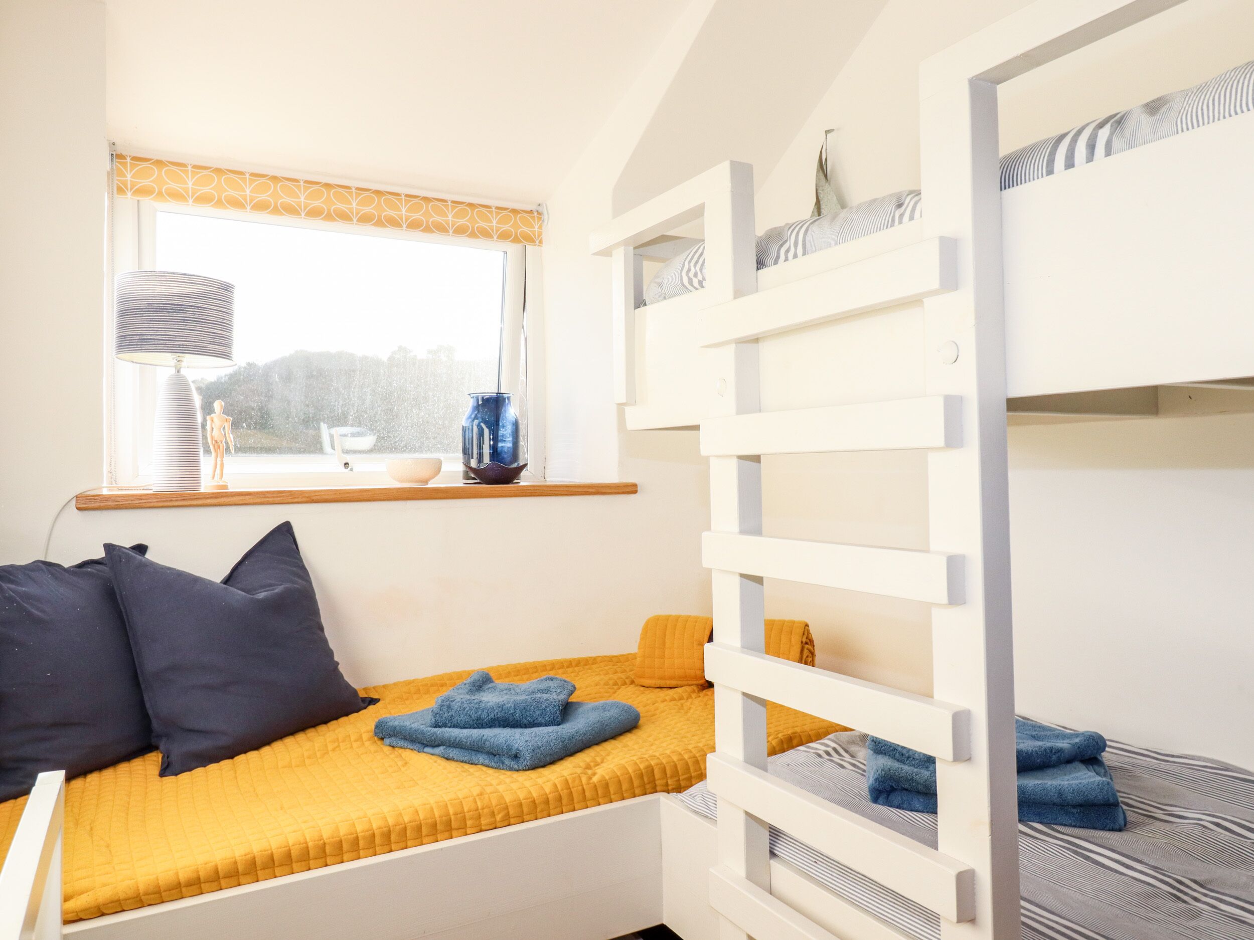 A bunk bed with a yellow bedspread, a window with a view, and a lamp on the windowsill.
