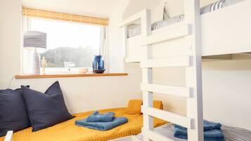 A bunk bed with a yellow bedspread, a window with a view, and a lamp on the windowsill.