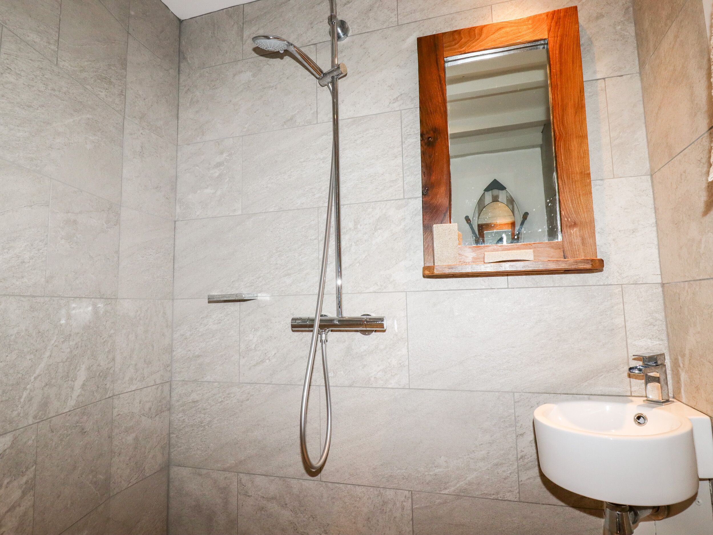 Un baño con ducha, lavamanos y espejo de marco de madera.