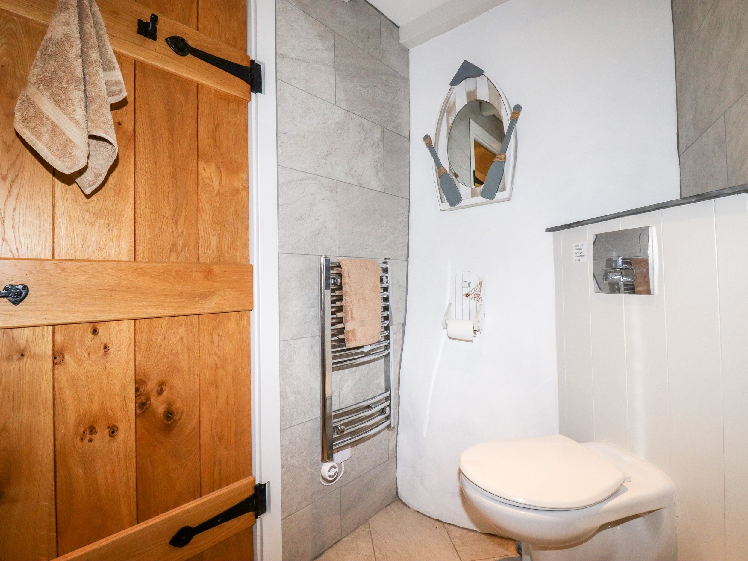 A bathroom with a wooden door, a towel rack, a mirror, a toilet, and a towel dispenser.