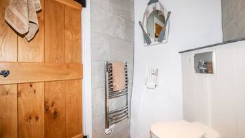 A bathroom with a wooden door, a towel rack, a mirror, a toilet, and a towel dispenser.