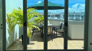 A balcony with a table and chairs, potted plants, and a green umbrella.