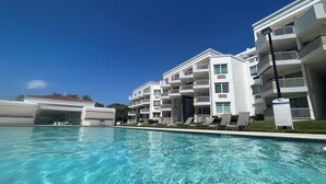 A modern hotel with a swimming pool, multiple balconies, and a clear blue sky.