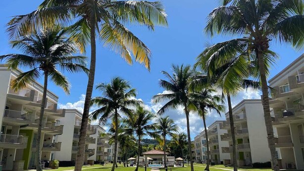 A resort with multiple-story buildings, a central pool area, and palm trees.