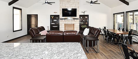 A spacious living room with a fireplace, leather sofas, a dining area with chairs, and a TV mounted on a stone wall.