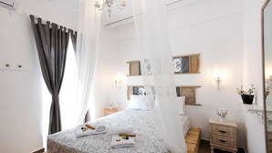 Une chambre à coucher comprenant un lit, des rideaux, une table de chevet, une commode, un miroir et des étagères fixées au mur.