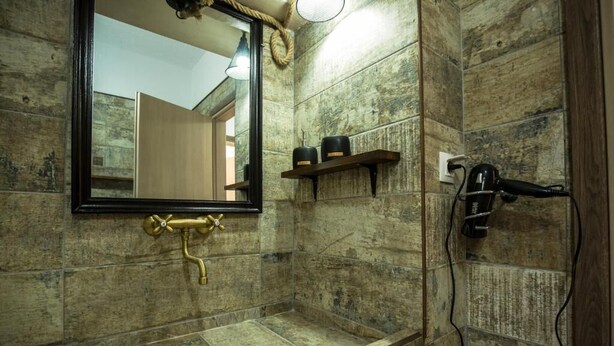 Une salle de bain avec un lavabo en pierre, un miroir et un sèche-cheveux posés sur une étagère fixée au mur.