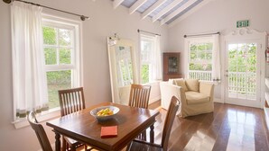 Un coin repas avec une table et des chaises en bois, un saladier rempli de fruits et une vue sur le jardin grâce à de grandes fenêtres.